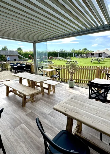 Covered café seating area with wooden tables overlooking a grassy outdoor play and picnic area.