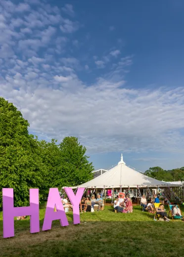 A large pink 'Hay' sign and a tent full of people in the background.