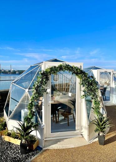 An outdoor dome housing a dining table and chairs overlooking the waterfront.