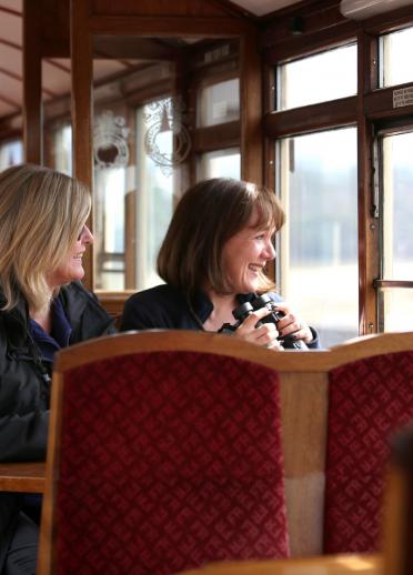 Two ladies sitting in the carriage on a steam train looking out the window.