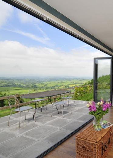 Wide open bifold doors reveal a vast view across a valley and fields.
