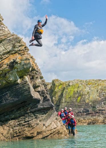 Male mid jump off rock, coasteering in Anglesey.