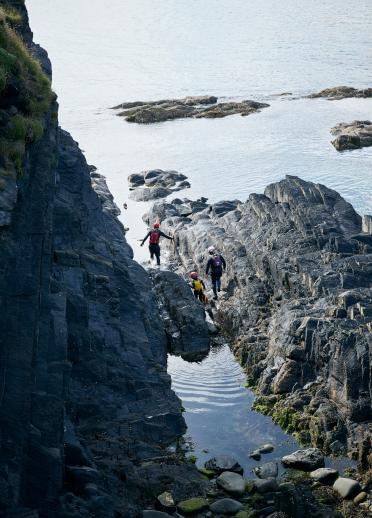 Family wading through large rocks off the West Wales coastline.