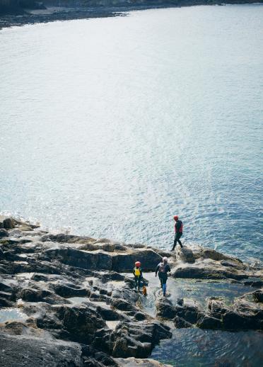 Coasteering on flat calm day, family exploring rocks infront of expanse of sea.