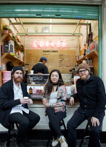 Eine Frau und zwei Männer sitzen vor einer Kaffeebude