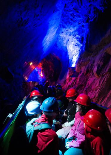 A group of people wearing hard hats exploring the colourful lit caves at King Arthur's Labyrinth.