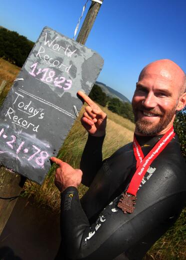 man in wetsuit with medal around his neck stood by chalk board.