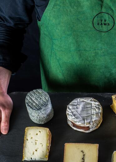 tray of cheeses being held with man's hand and apron.