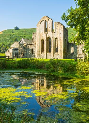 The ruins of an old abbey, with reflection in water, on a sunny day.