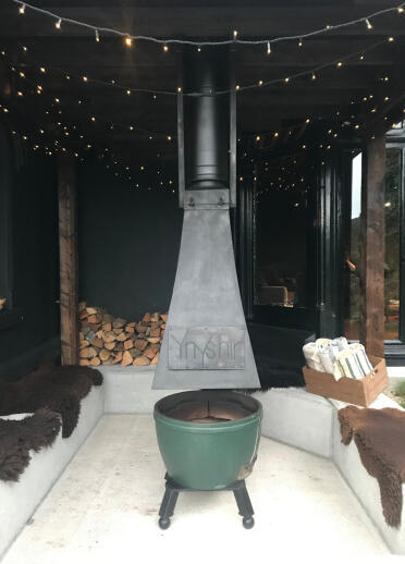 A firepit under an outdoor shelter, with seating around. 