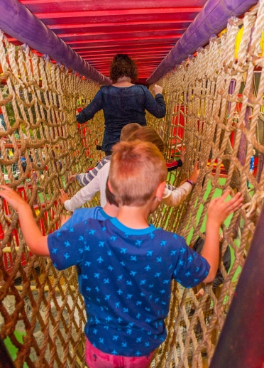 children walking on rope bridge indoor play facility.