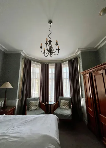 Interior of accessible twin bedroom with two armchairs, and a chandelier-style light hanging from the high ceiling.