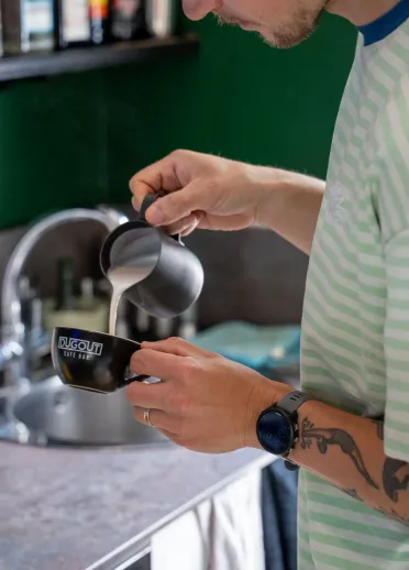 Barista pouring hot milk into a coffee cup