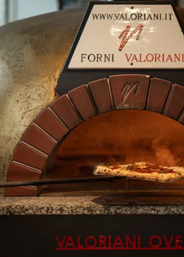 A pizza being placed in the woodfire pizza