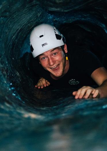 A man crawling through a manmade cave wearing safety gear in an adventure park.