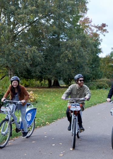 Three people on bicycles, cycling through a park.