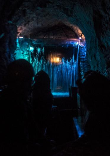 People underground on a boat approaching a lit up waterfall.