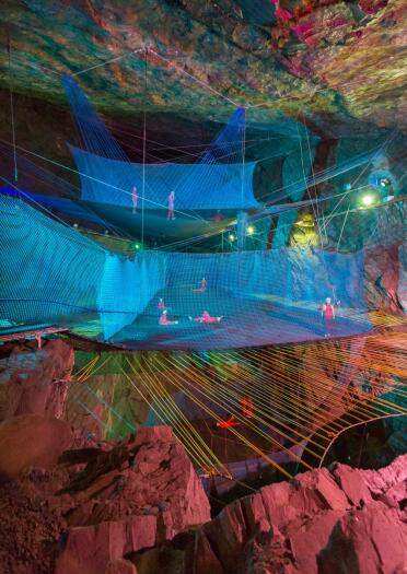 People playing on a series of play nets suspended in an underground cavern.