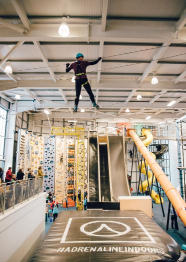 An adventurer crossing over the high wire in front of slides and climbing frames.