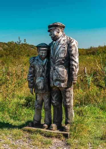 Statue of a man comforting a boy surrounded by wild meadowland
