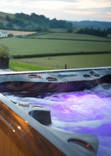 A bubbling hot tub on a terrace with views across field.