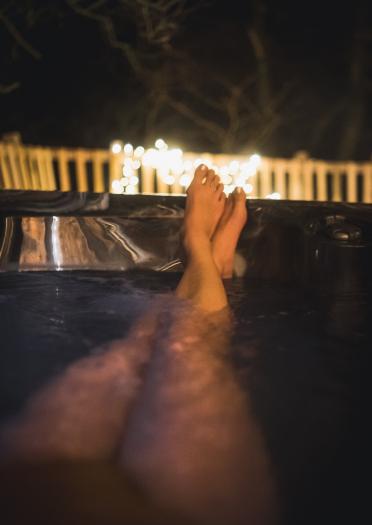 Close up of a woman's feet relaxing in a hot tub with flickering candles in the background.