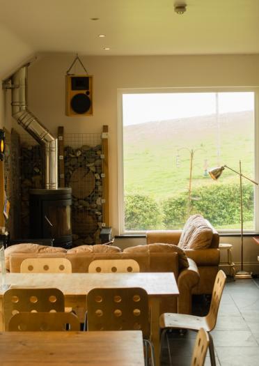 The interior of an eco lodge with a coal fire, sofas and views out the hills.