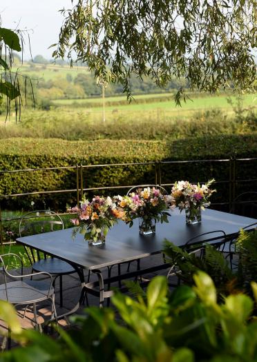 An outdoor seating area with vases of flowers overlooking green pastures and hills.