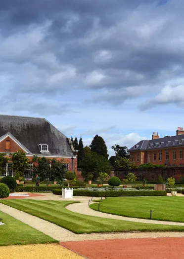 Lawned gardens, footpaths and trimmed topiary outside a grand house.