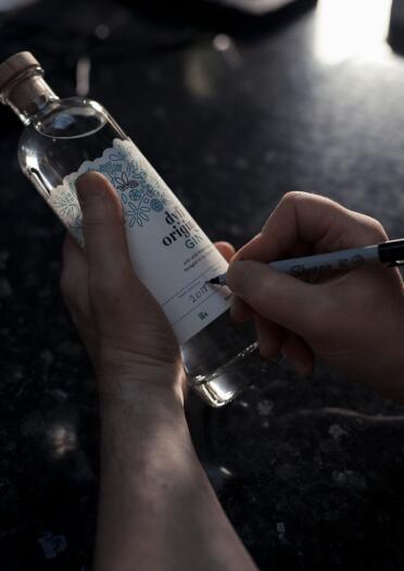 Ein Mann schreibt das Destillationsdatum auf eine Flasche Gin.