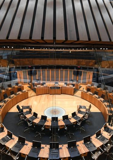 Chairs and tables set in a circle inf the debating chamber of a parliament building.