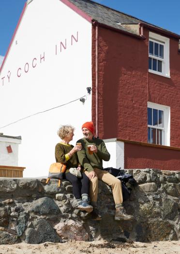 Couple sitting on a wall enjoying a drink outside the Ty Coch Inn.