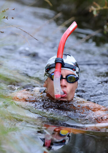 A person with a snorkel swimming in a bog.