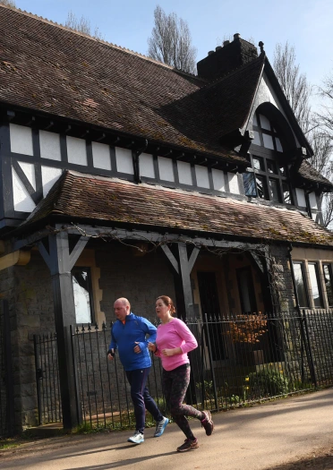 Two runners running past a Tudor house in Bute Park.
