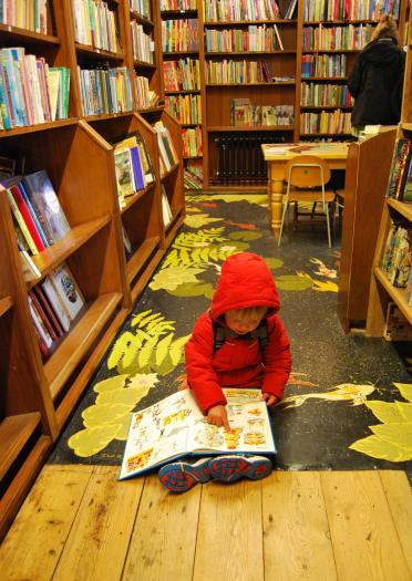 A small child reading a book on the floor of a book shop.