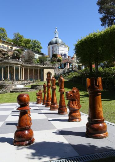 Große hölzerne Schachfiguren auf einem riesigen Schachbrett in einer Gartenanlage von Portmeirion.