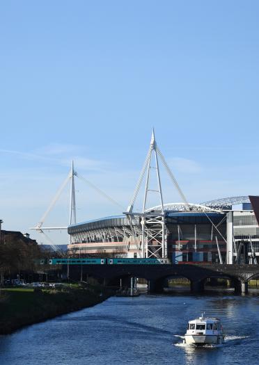 A river with a boat and a large sports stadium behind.
