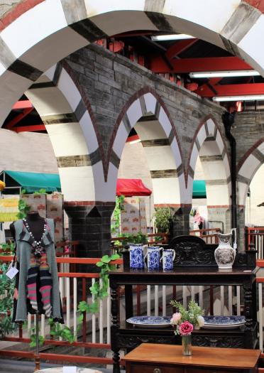 interior archways with tables and plants in the foreground and a crafted dolphin hanging up in the background and market stall roofs