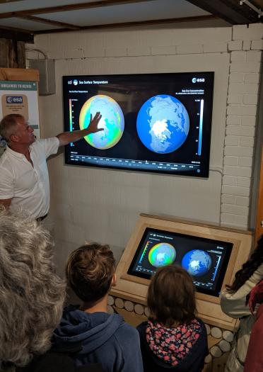 A man explaining a screen image of two globes to an audience.