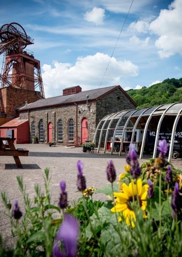 Exterior of mining attraction and colliery tower with flowers in foreground.