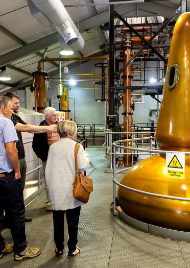 Eine Besuchergruppe bei einer Führung durch die Penderyn Distillery mit einem Führer, der die goldgelben Fässer betrachtet.