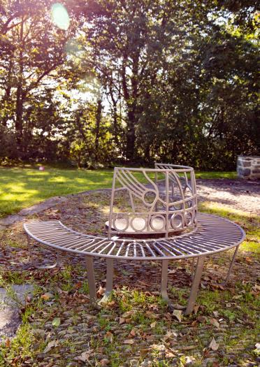 Art installation in the shape of a metal, circular bench in a garden with trees in the background