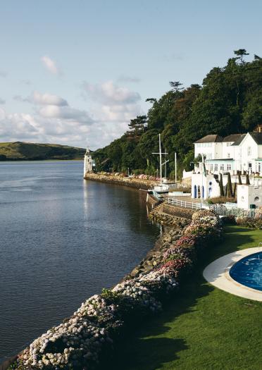A white-fronted hotel and outdoor swimming pool by a river.