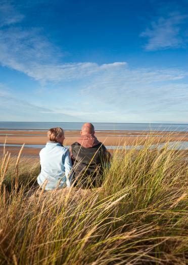 Woman and man sitting on sand dunes looking out to sea
