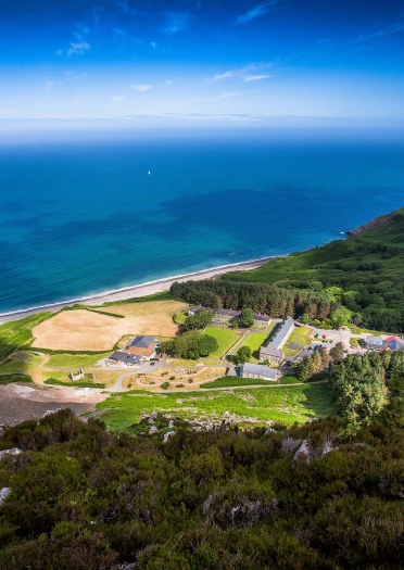 Luftaufnahme von Nant Gwrtheyrn inmitten grüner Landschaft am Meer.