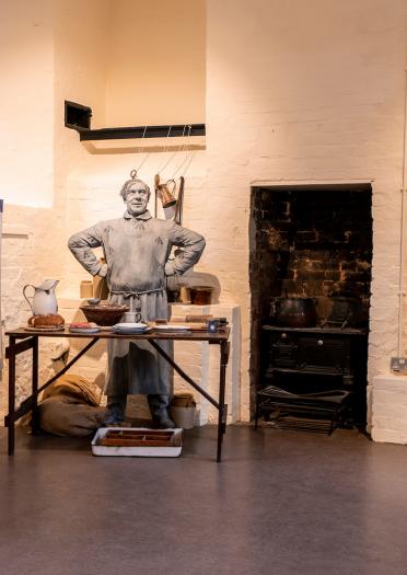 A display at Ruthin Gaol showing a figure behind a table with kitchen equipment.
