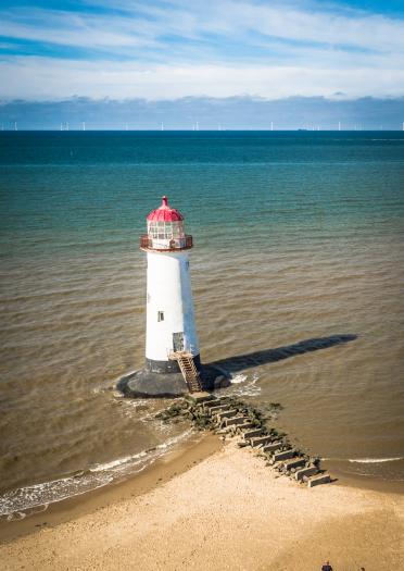 A white lighthouse off a sandy beach.