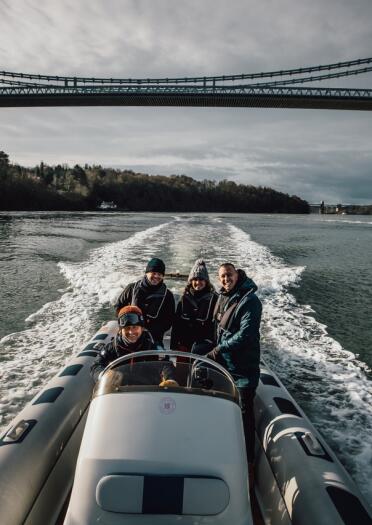 Four people on a boat ride with the Menai Bridge behind them