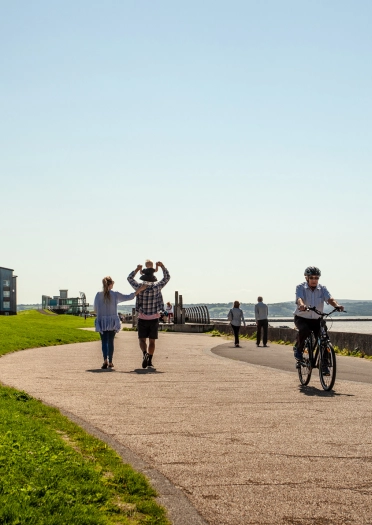 Spaziergänger und Radfahrer auf einem breiten Weg am Meer.