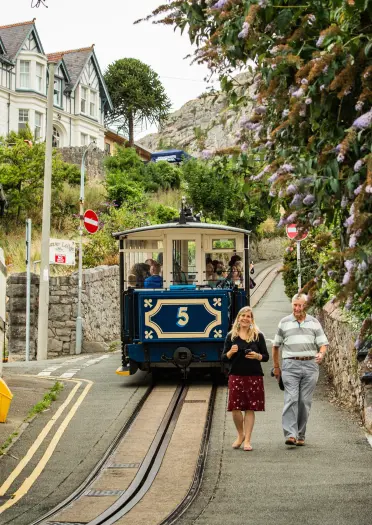 Tram coming down the road with two people walking beside it